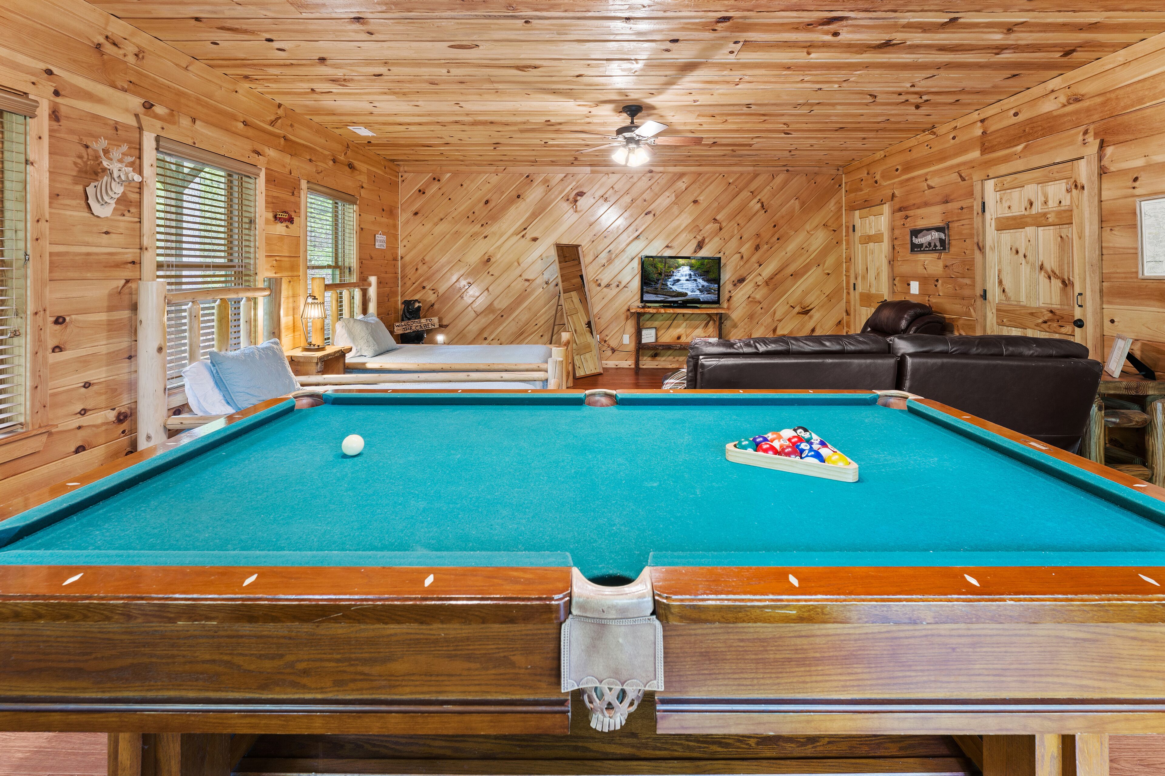 A pool table with a ball, a television, and a sofa in a wooden room.