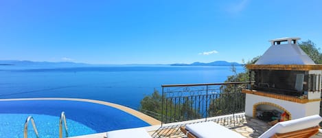A poolside area with lounge chairs, a barbecue, and a view of the sea.