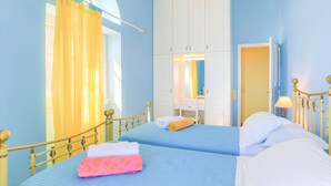 Una habitación con dos camas, una ventana con cortinas amarillas, un armario blanco y una mesita de noche con lámpara.