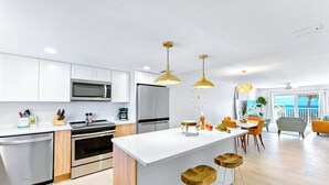 A modern kitchen with white cabinets, stainless steel appliances, and wooden bar stools. - Stylish Beachfront Condo – Balcony, Heated Pool & Steps to Pier (Cocoa Beach)