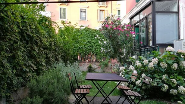 A patio with a table and chairs, surrounded by greenery and a view of buildings. - GuestHost - Cozy apartment in Dorsoduro with GARDEN! (Venezia)