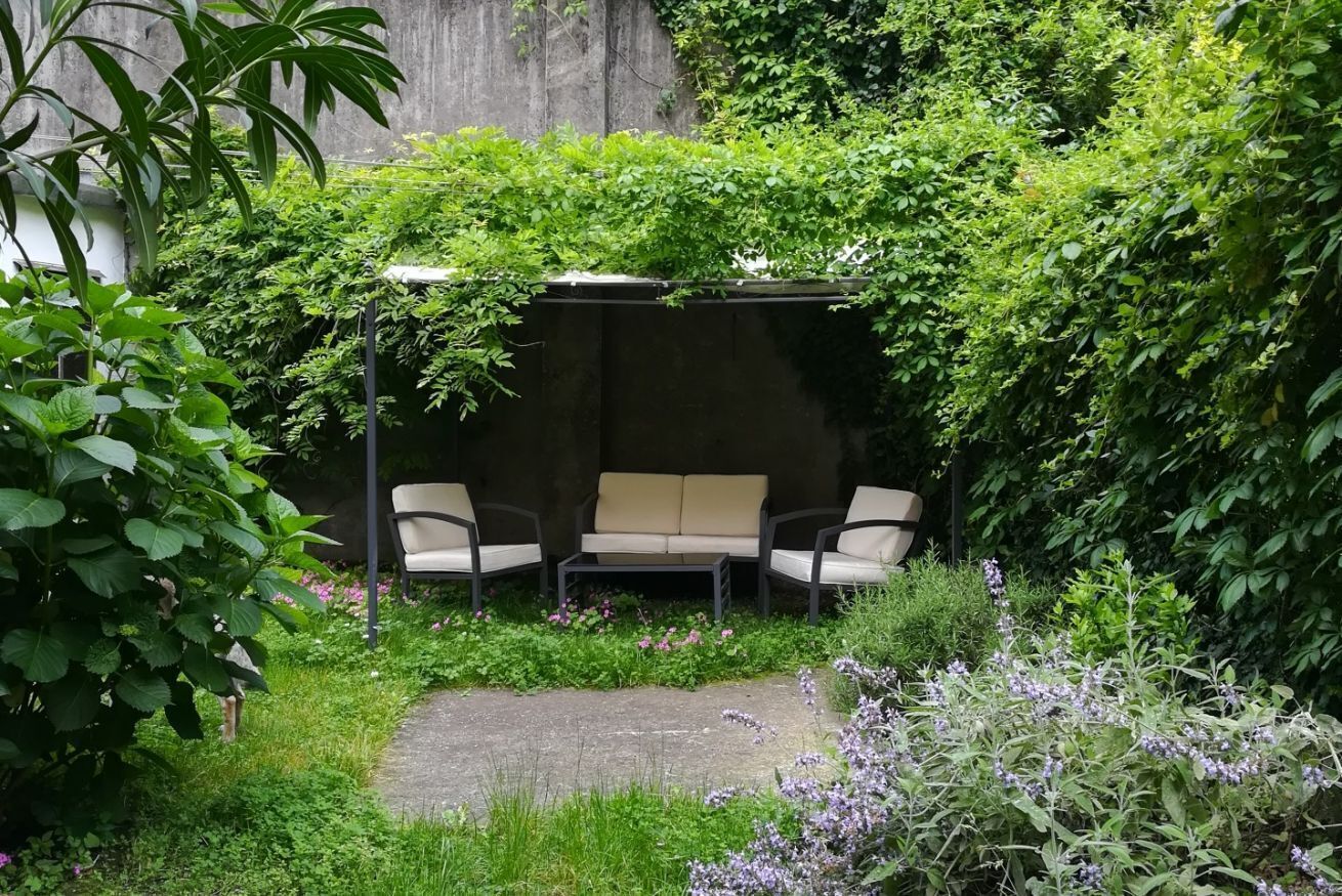 Un jardin agrémenté d’un espace détente, d’un chemin en béton et d’une végétation luxuriante.