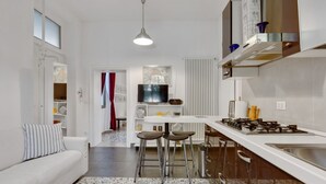 A modern kitchen with a gas stove, bar stools, and a dining area with a white table. - GuestHost - Cozy apartment in Dorsoduro with GARDEN! (Venezia)