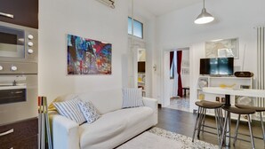 A modern kitchen with built-in appliances, a dining area with bar stools, and a living space with a sofa and artwork. - GuestHost - Cozy apartment in Dorsoduro with GARDEN! (Venezia)