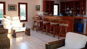 Une cuisine avec des meubles en bois, un coin bar avec des chaises en osier et un coin repas avec des meubles en osier.