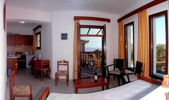 Habitación de hotel con cama, zona de comedor con sillas, cocina y vistas al exterior.