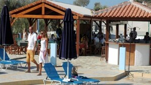 Un espace extérieur abrité avec des chaises longues et des parasols, un coin bar où se trouvent des personnes, et une zone dédiée à la piscine.