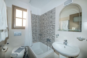 A bathroom with a bathtub, a sink, a mirror, and a window.
