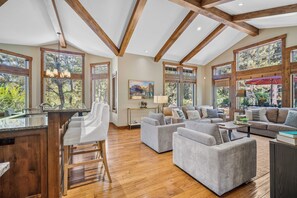 A spacious living area with a wooden ceiling, large windows, and a kitchen area with a bar.