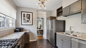 A modern kitchen with a stainless steel refrigerator, granite countertops, and a gas stove. - Renovated Jones Street Parlor Apt +Private Parking (Savannah)