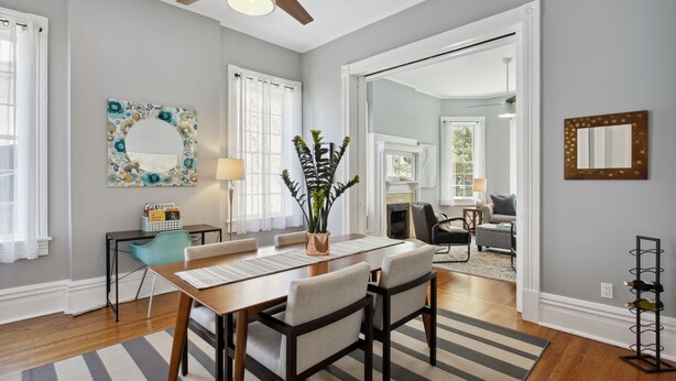 A dining area with a wooden table, chairs, a striped rug, a ceiling fan, and a fireplace. - Renovated Jones Street Parlor Apt +Private Parking (Savannah)