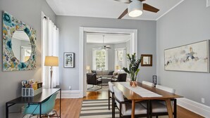 A modern living room with a dining area, a ceiling fan, and a large window. - Renovated Jones Street Parlor Apt +Private Parking (Savannah)