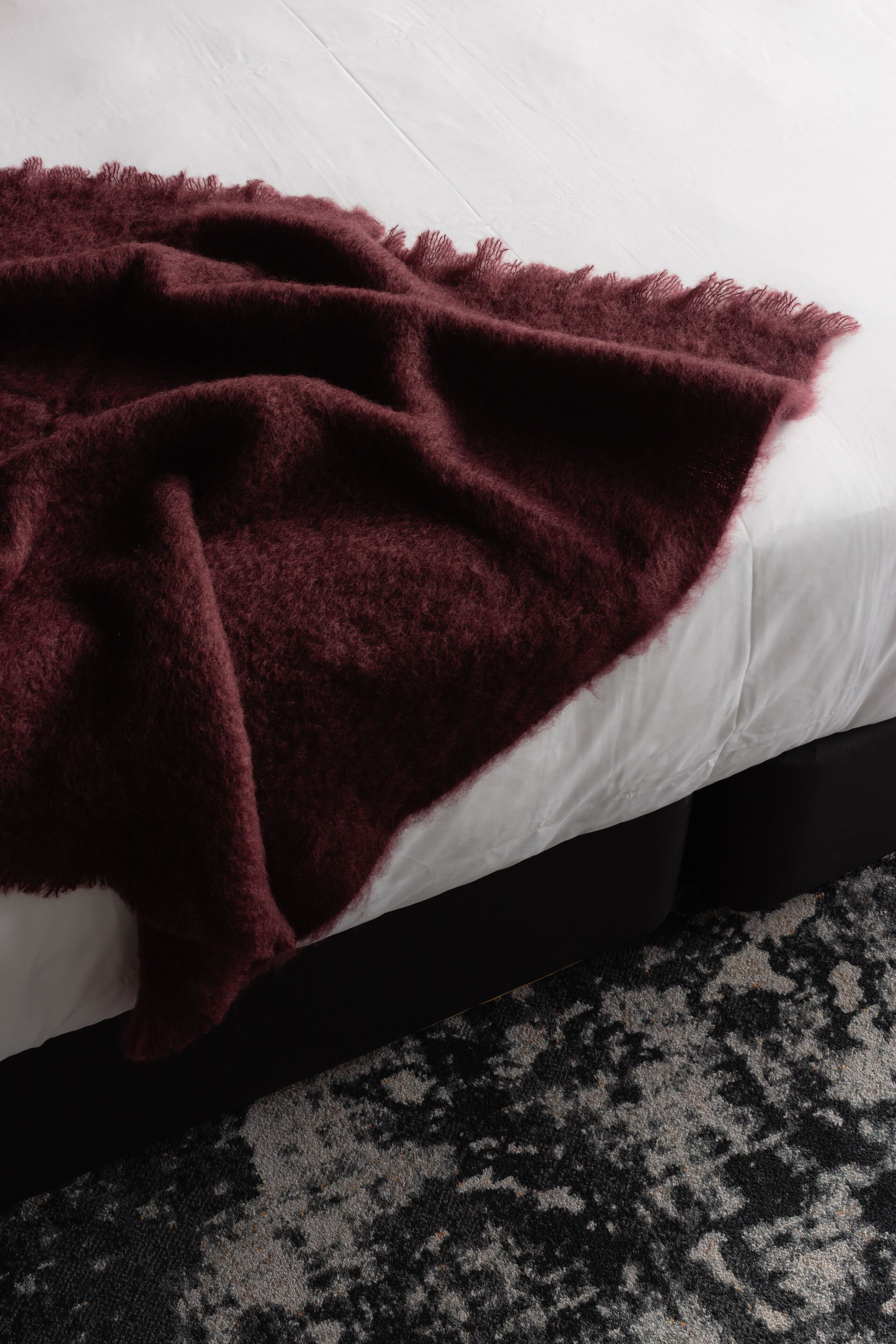 A bed with a white mattress and a dark-colored blanket.