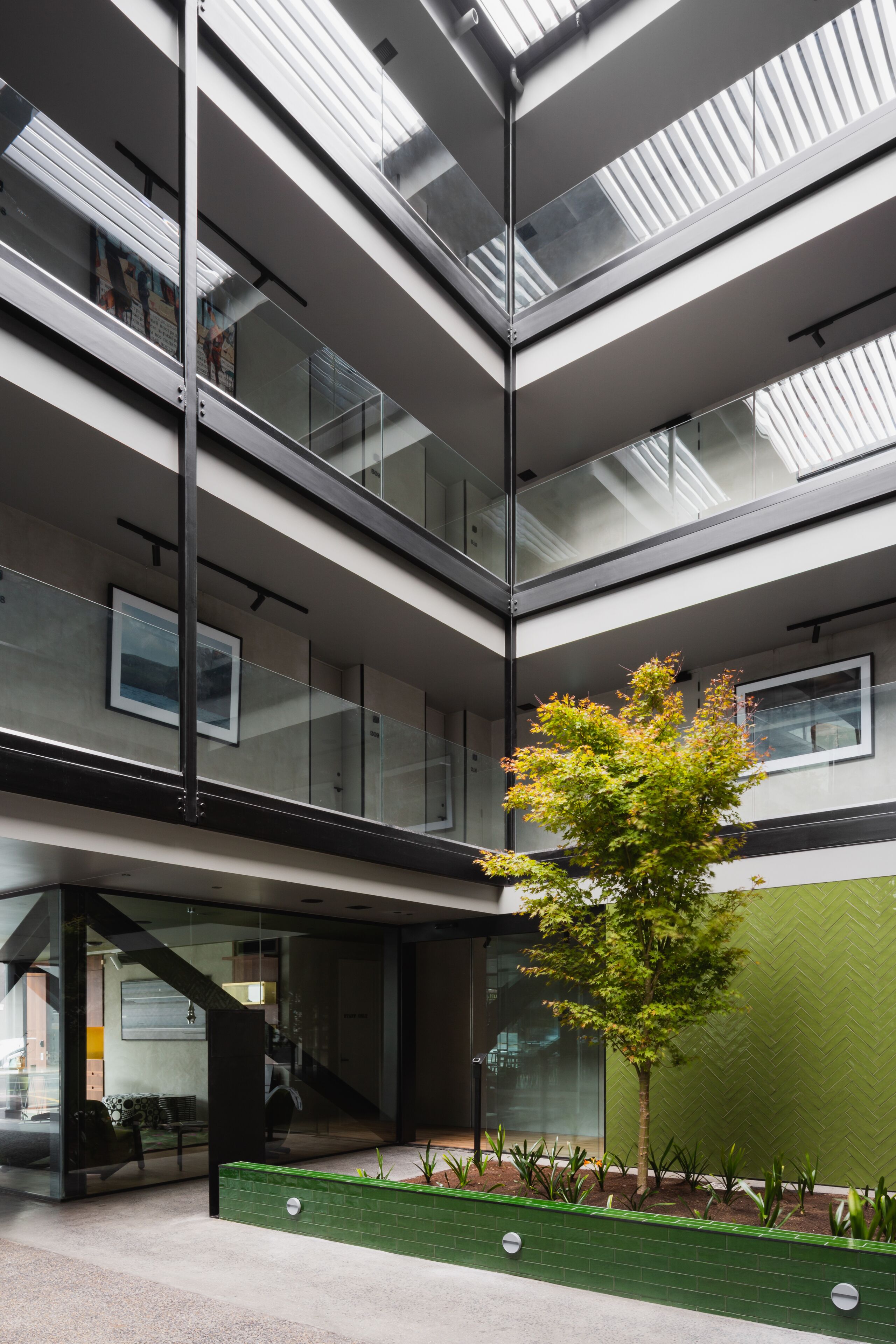 A multi-level atrium with glass railings, a central staircase, and a small tree in a planter.