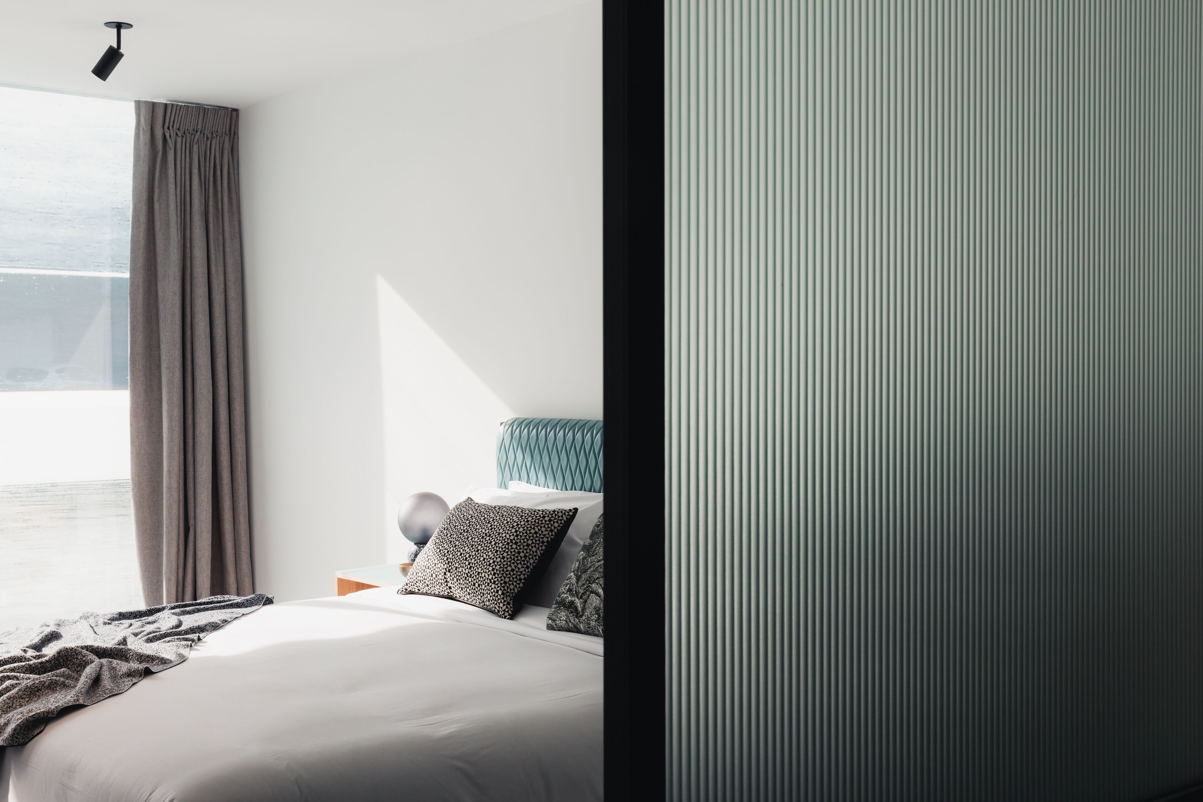 A modern bedroom with a large window, a bed with multiple pillows, and a nightstand.