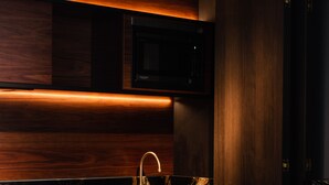 A modern kitchen with dark wood cabinetry, a stainless steel sink, and a microwave above it. - Ebb-Dunedin (Dunedin)