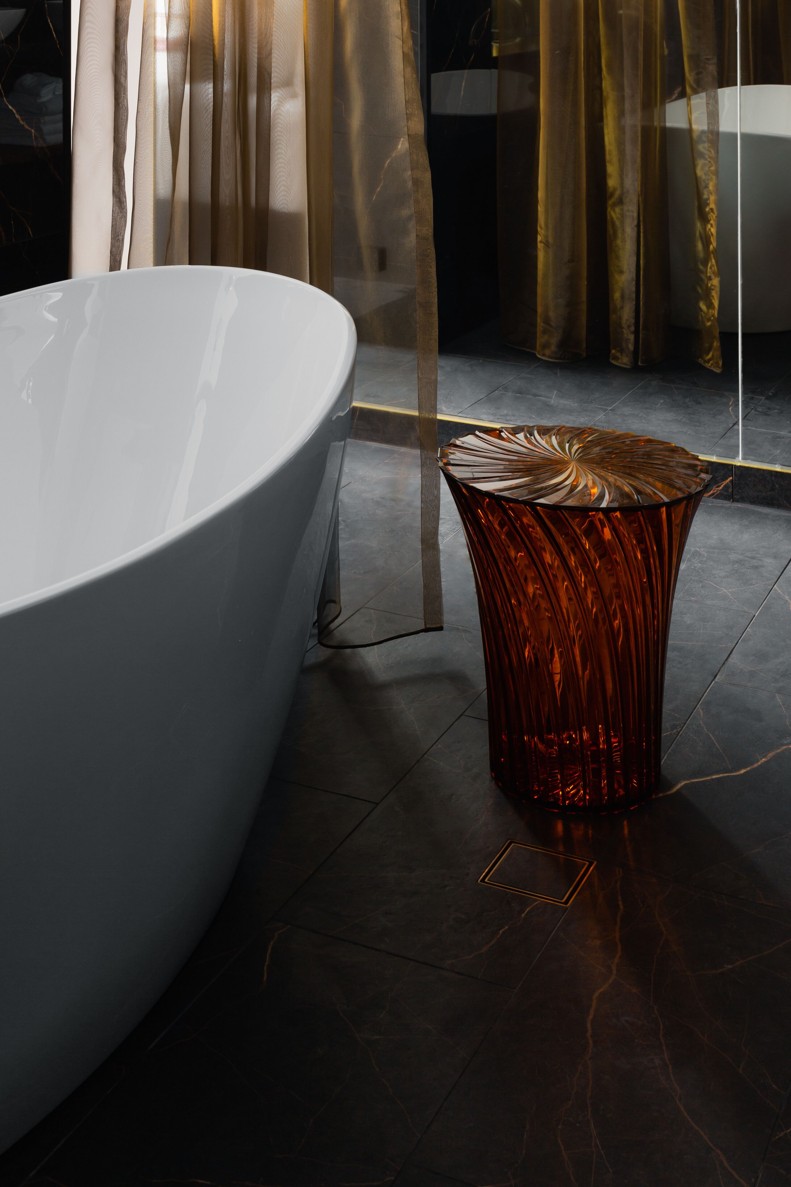 A modern bathroom with a large white bathtub, a textured glass stool, and a floor with a subtle pattern.