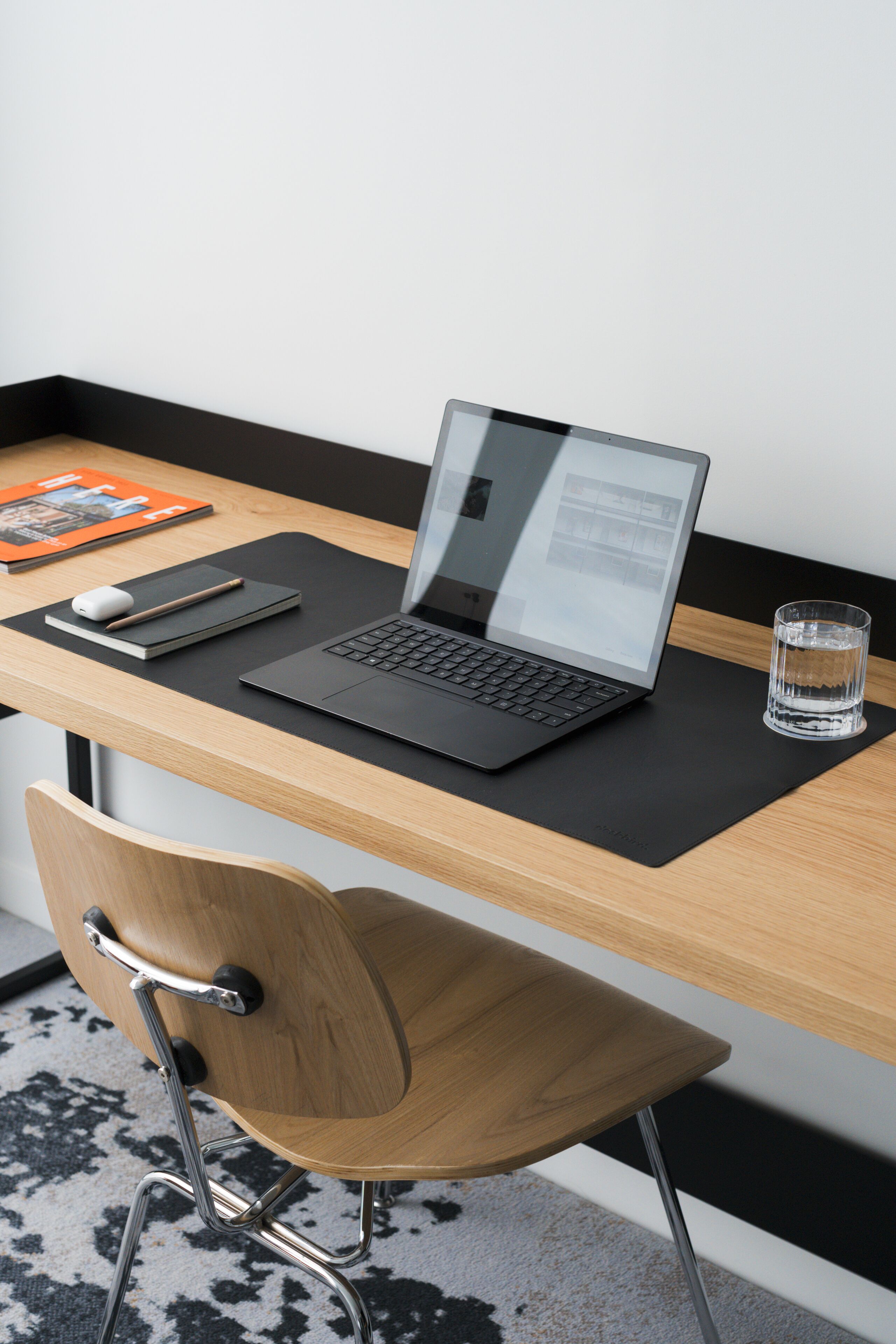 A laptop on a wooden desk with a glass of water, a notebook, and a mouse.