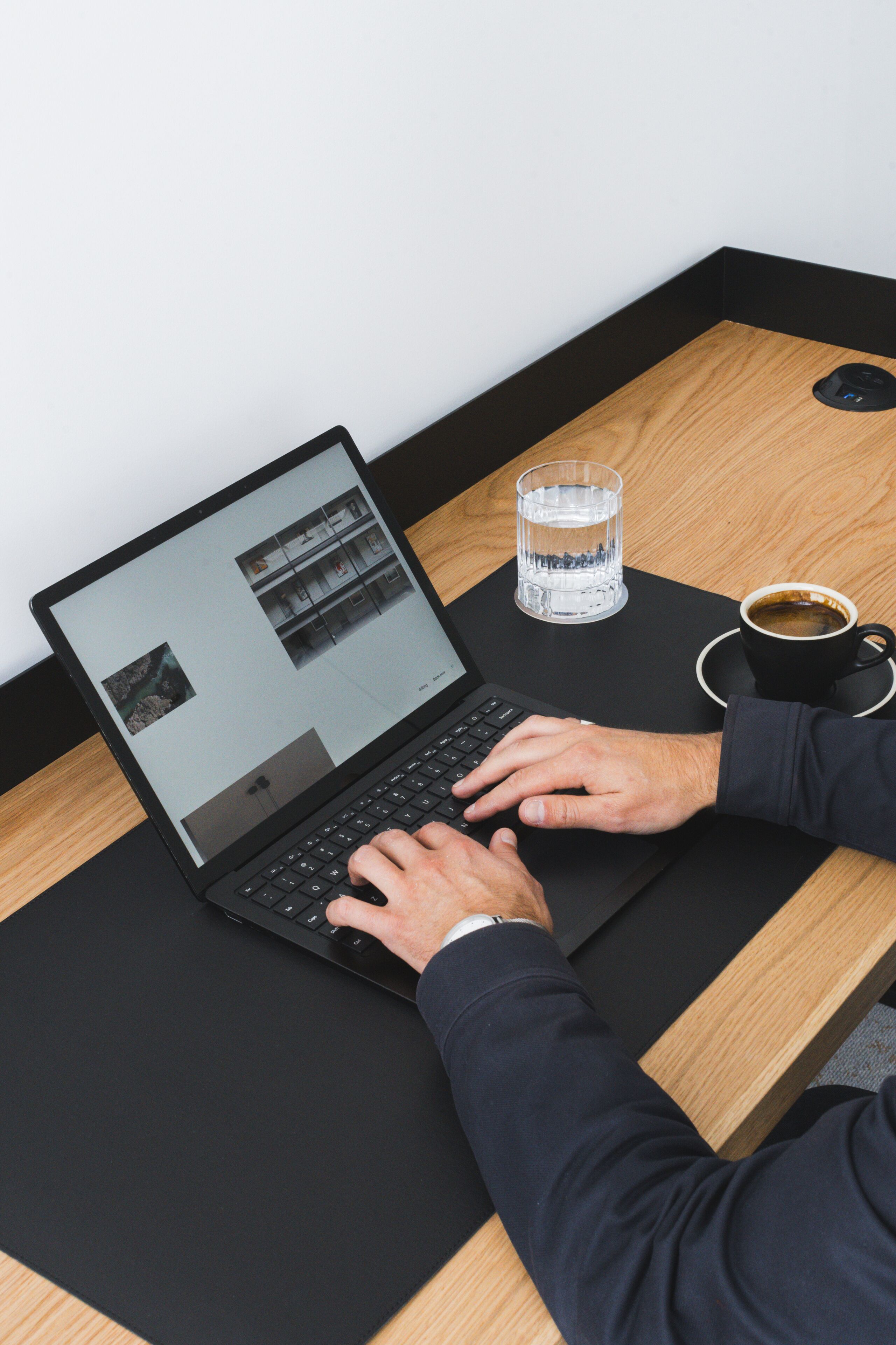 A laptop on a wooden table with a glass of water and a cup of coffee.