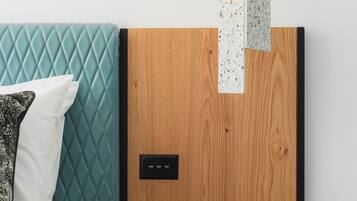 Un dormitorio moderno con un cabecero acolchado color turquesa, un panel de madera en la pared, una mesita de noche con un vaso de agua y una revista.