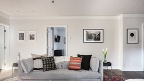 Ein modernes Wohnzimmer mit einem grauen Sofa, einem Couchtisch mit Büchern und Snacks sowie gerahmten Bildern an den Wänden.