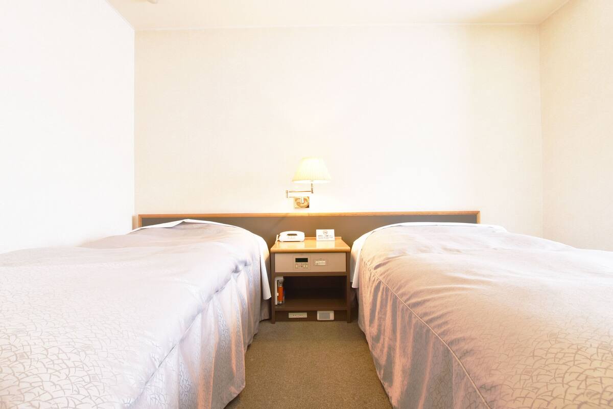Een hotelkamer met twee éénpersoonsbedden, een nachtkastje met een lamp, een kleine tafel en een ladekast.
