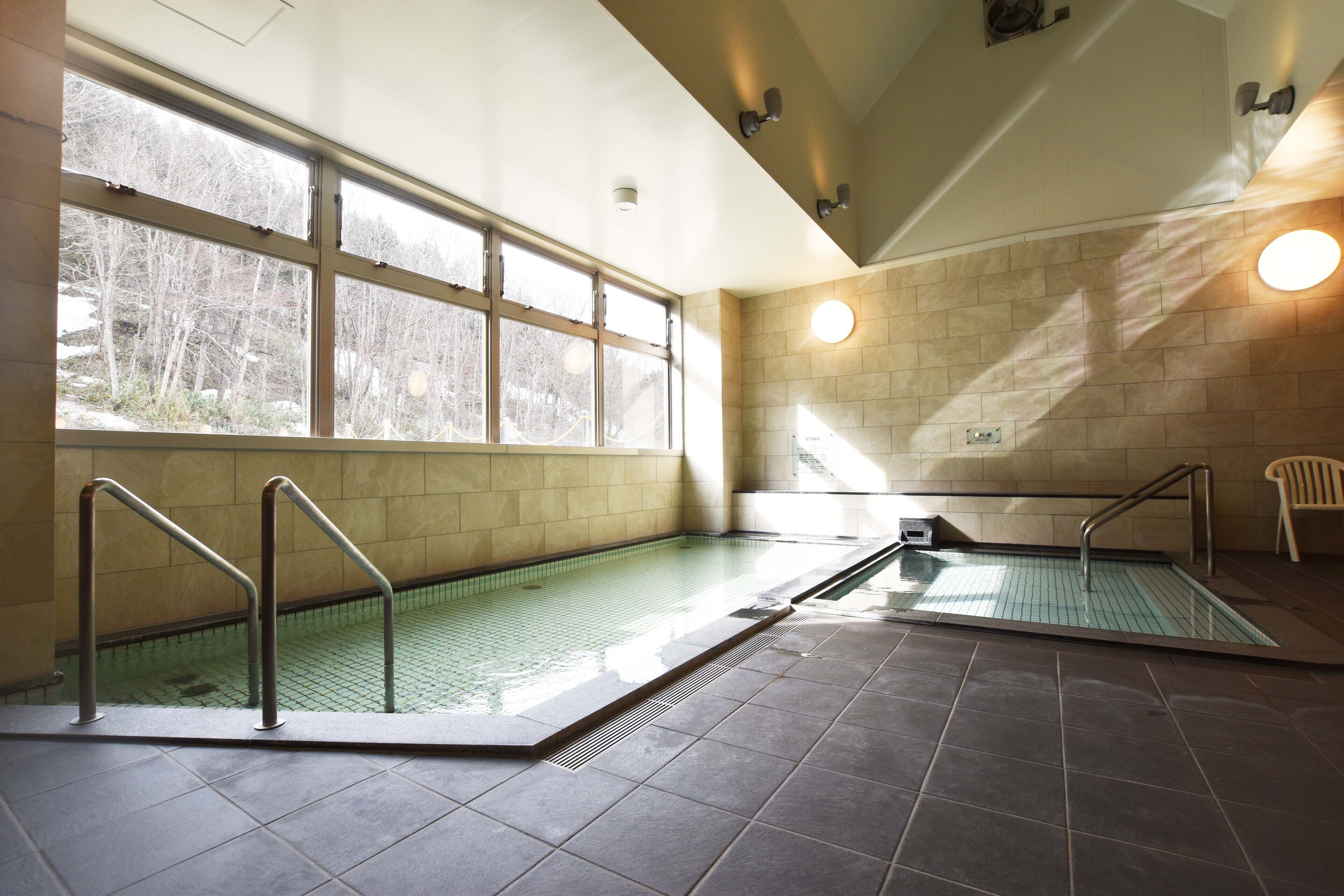 An indoor swimming pool with clear glass walls, metal railings, and a view of trees outside.