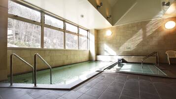 An indoor swimming pool with clear glass walls, metal railings, and a view of trees outside.