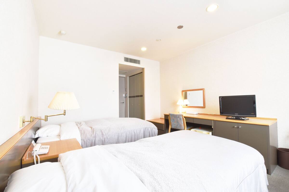 Een hotelkamer met twee bedden, een bureau met computer en televisie, een lamp en een telefoon op het nachtkastje.