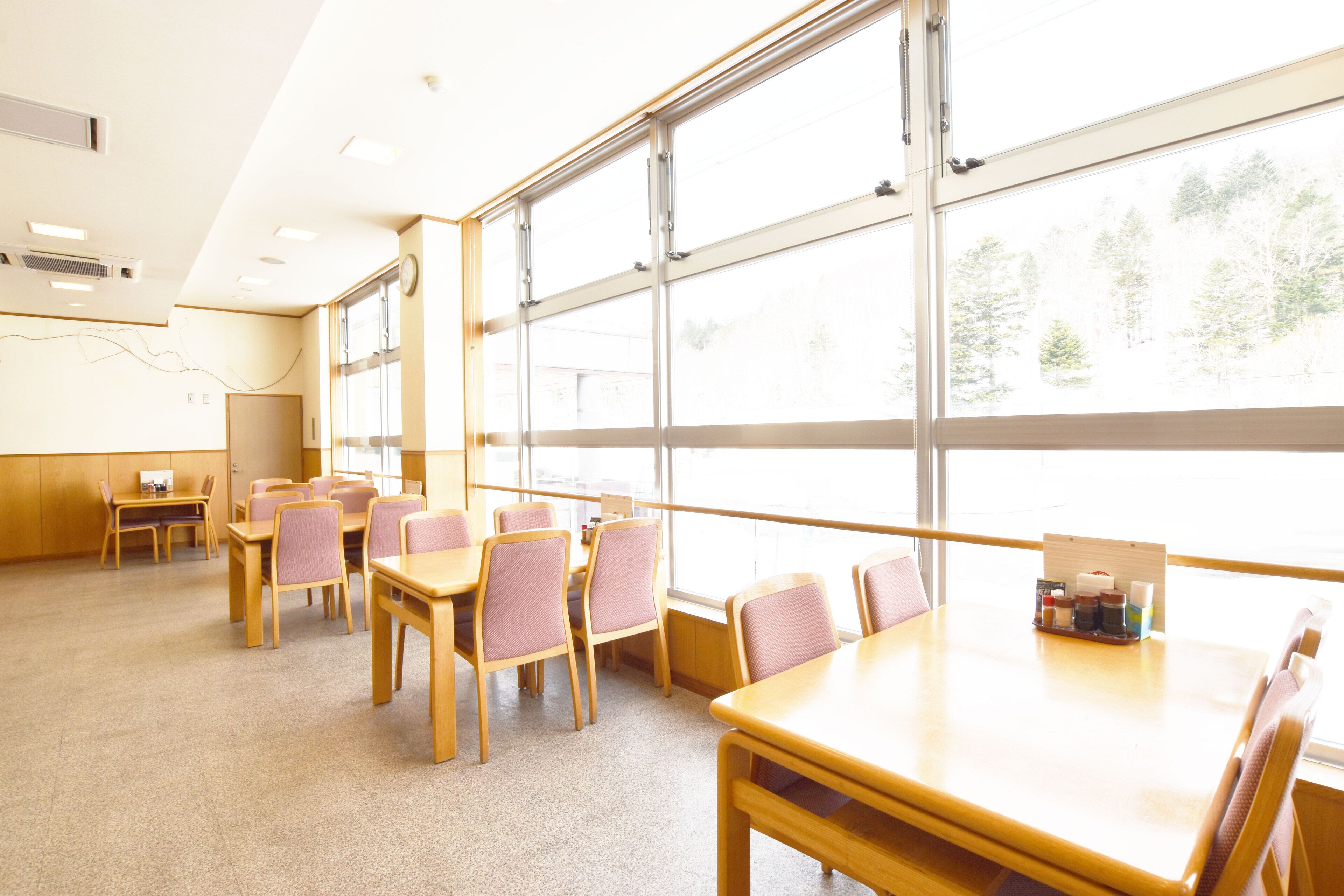 A spacious room with large windows, wooden tables and chairs, and a small table with a tray of items.