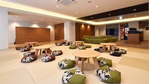 Un hall d’entrée spacieux avec plusieurs coins salon, comprenant des tables rondes et des fauteuils en forme de poire, ainsi qu’un canapé vert.