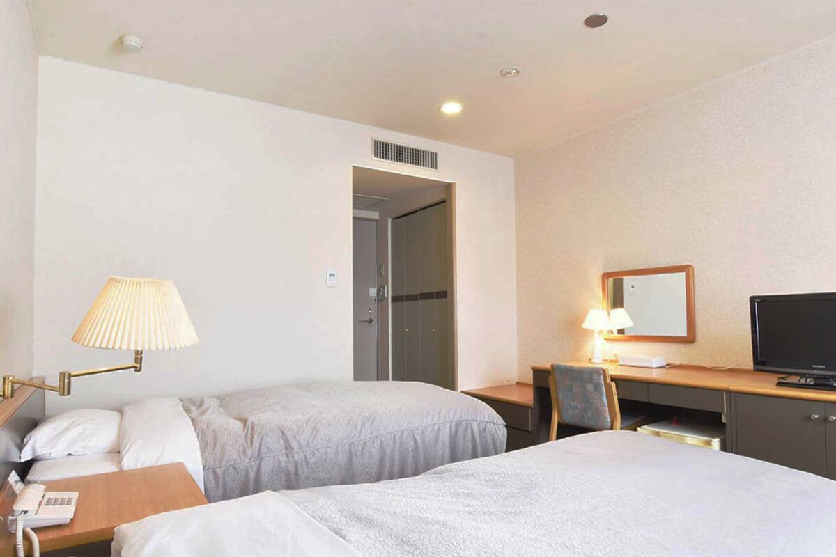 Een hotelkamer met twee bedden, een bureau met een televisie, een lamp en een telefoon.