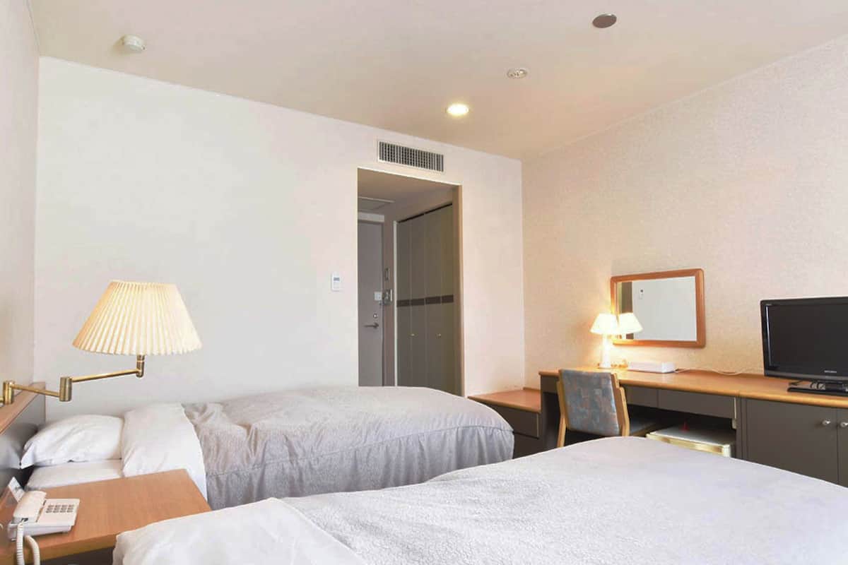 Una habitación de hotel con dos camas, un escritorio con televisor, una lámpara y un teléfono.