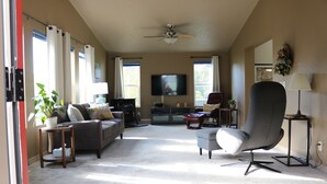 Un salón amplio con un sillón gris, un sofá y un televisor en la pared.