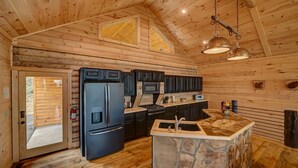 A wooden cabin interior with a kitchen featuring a stone island, black appliances, and a large window. - Serenity Peak | Mountain View | Close To Town | Paved | Dog Friendly (Blue Ridge)