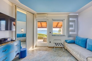A modern room with a sofa, a TV, a dresser, and a view of the sea.
