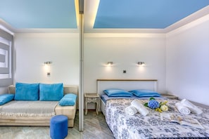 A bedroom with a sofa, a bed with a patterned bedspread, and two bedside tables with lamps.