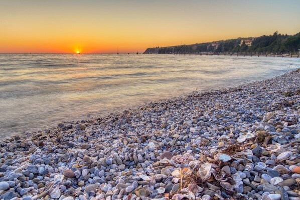 Una playa de guijarros con un atardecer al fondo.