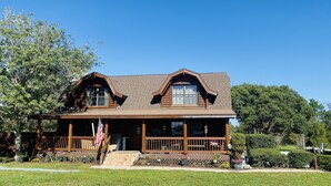 A log cabin with a porch and a flag, surrounded by greenery.