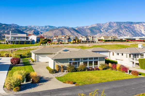 A residential area with modern houses, a well-maintained lawn, and a mountain backdrop.