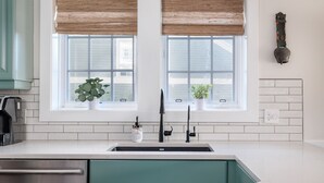 A kitchen with a sink, two windows with blinds, a potted plant, and a wall-mounted light fixture.