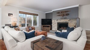 A living room with a stone fireplace, a large window, and a flat-screen TV.
