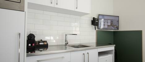 A modern kitchen with white cabinets, a stainless steel sink, and a coffee machine.