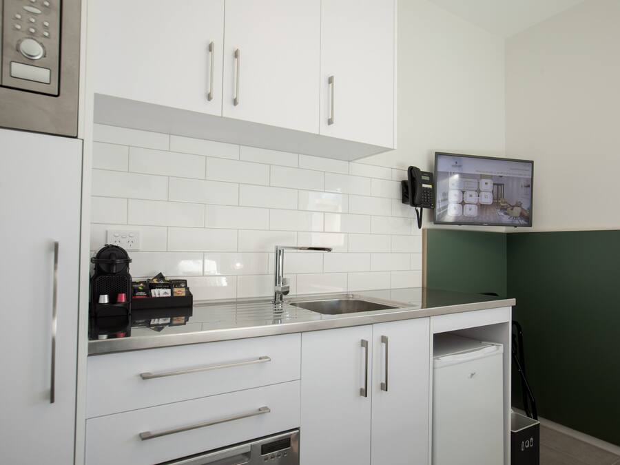 A modern kitchen with white cabinets, a stainless steel sink, and a coffee machine.