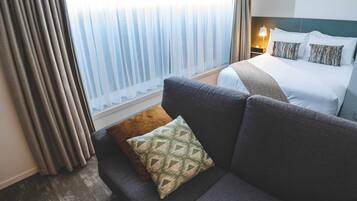 A hotel room with a bed, a sofa, and a window with curtains.