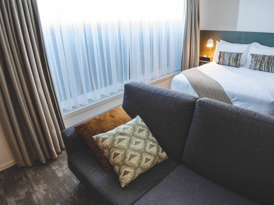 Une chambre d’hôtel avec un lit, un canapé et une fenêtre avec des rideaux.