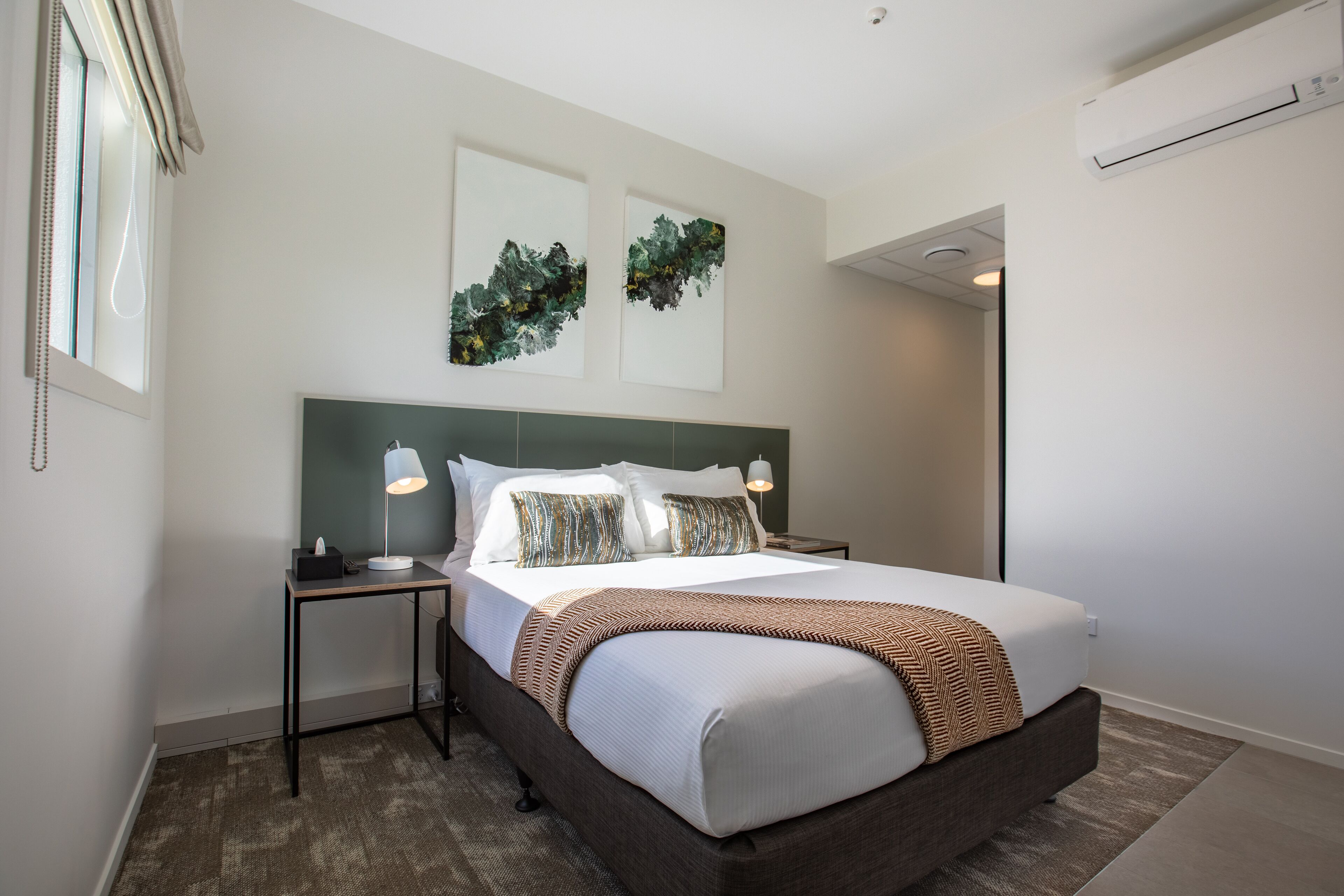 Una habitación de hotel moderna con una cama grande, dos mesitas de noche y un aire acondicionado instalado en la pared.