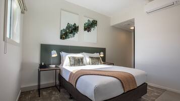 Una habitación de hotel moderna con una cama grande, dos mesitas de noche y un aire acondicionado instalado en la pared.