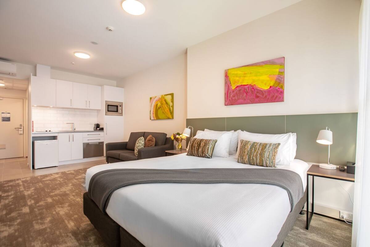 Una habitación de hotel con una cama grande, un sofá, una zona de comedor y una cocina.