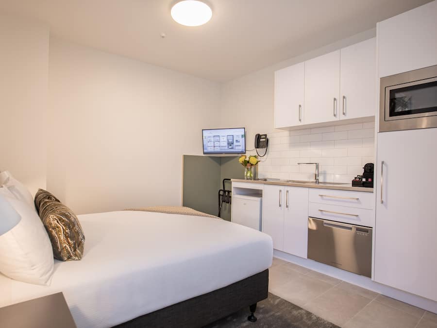 Une chambre d’hôtel moderne équipée d’un lit, d’une lampe de chevet et d’une petite kitchenette avec un four à micro-ondes et un lave-vaisselle.